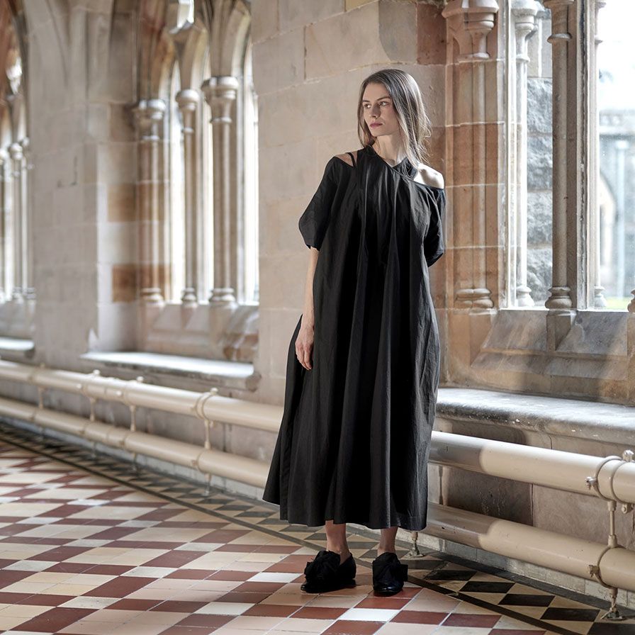 Frau in langem schwarzem Kleid mit Kapuze in historischer Architektur.