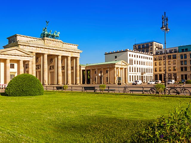 Brandenburger Tor in Berlin mit neoklassizistischem Bau und grünem Vorplatz unter blauem Himmel.