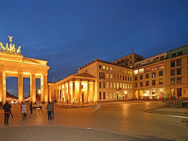 Brandenburger Tor in Berlin bei Nacht mit beleuchtetem Umfeld und Besuchern.