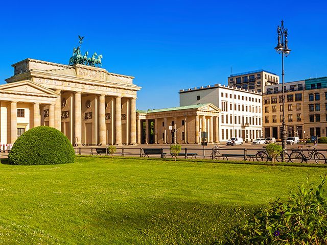 Brandenburger Tor in Berlin mit neoklassizistischem Bau und grünem Vorplatz unter blauem Himmel.