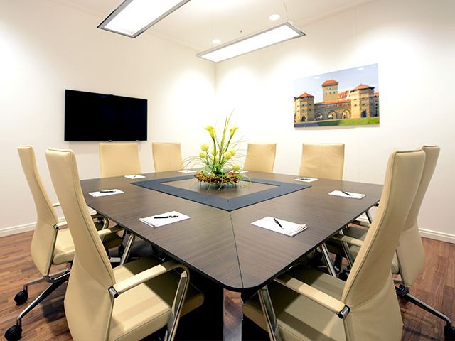Moderner Konferenztisch mit acht Stühlen, Blumenarrangement und TV an der Wand.