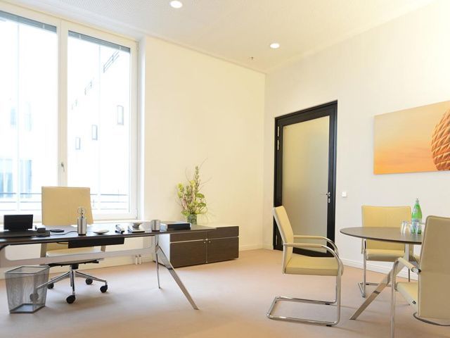 Moderne Büroumgebung mit Schreibtisch, Besprechungstisch und großem Fenster.