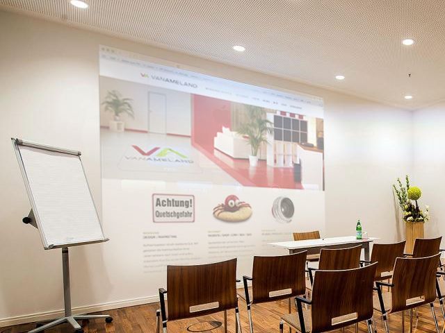 Moderner Seminarraum mit Projektor, Flipchart und Tischen für Präsentationen.